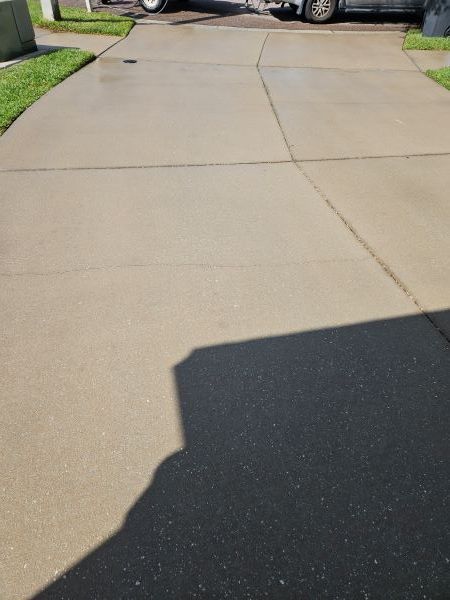 Concrete driveway with cracks and a parked vehicle in the distance, bordered by grass and sidewalks