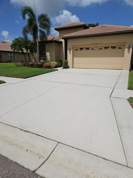 Beige house with light gray concrete driveway and green lawn under a sunny blue sky.
