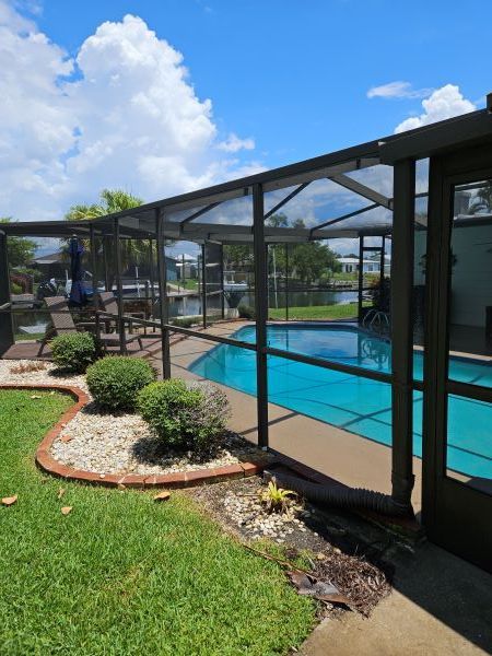 Pool enclosed by a screened lanai; blue water, green grass, and sunny sky.