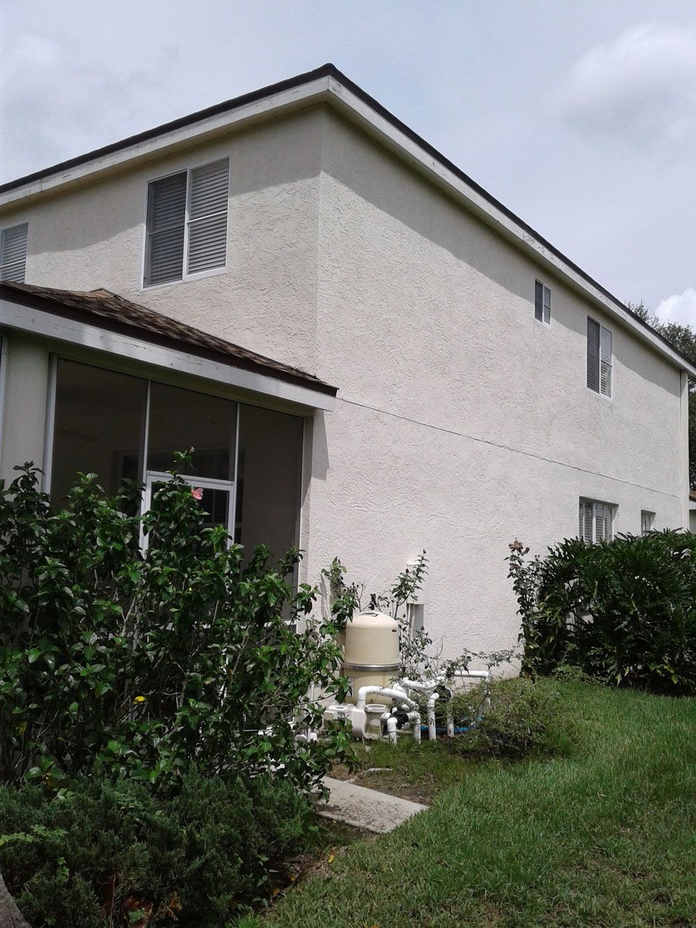 Side view of a beige stucco house with a small porch, shrubs, and a green lawn.