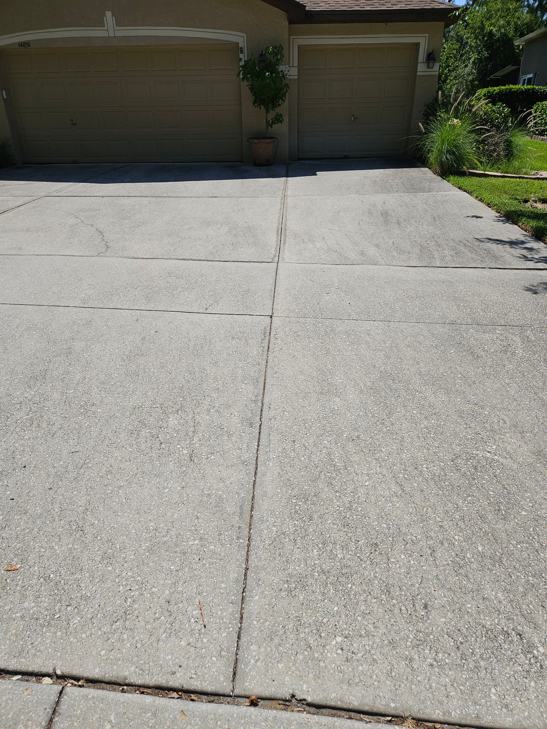 A concrete driveway in front of a house with two garage doors.