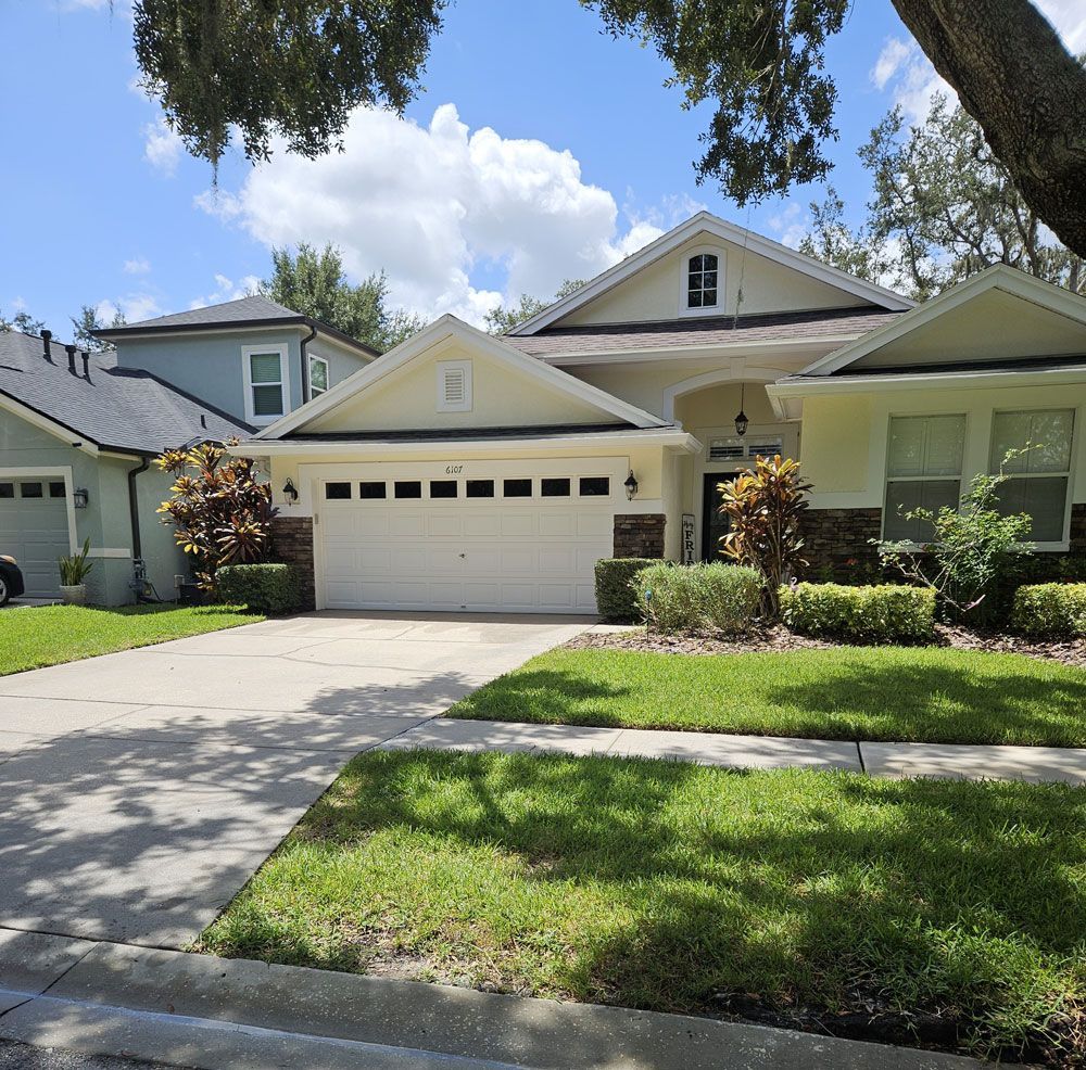 Suburban house with a white garage, driveway, green lawn, and trees in front