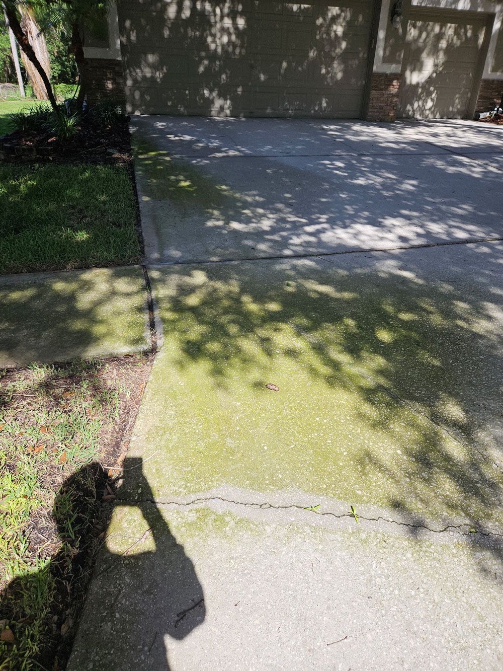 Sunlit driveway beside a grassy lawn, with tree shadows and a person’s shadow in the foreground