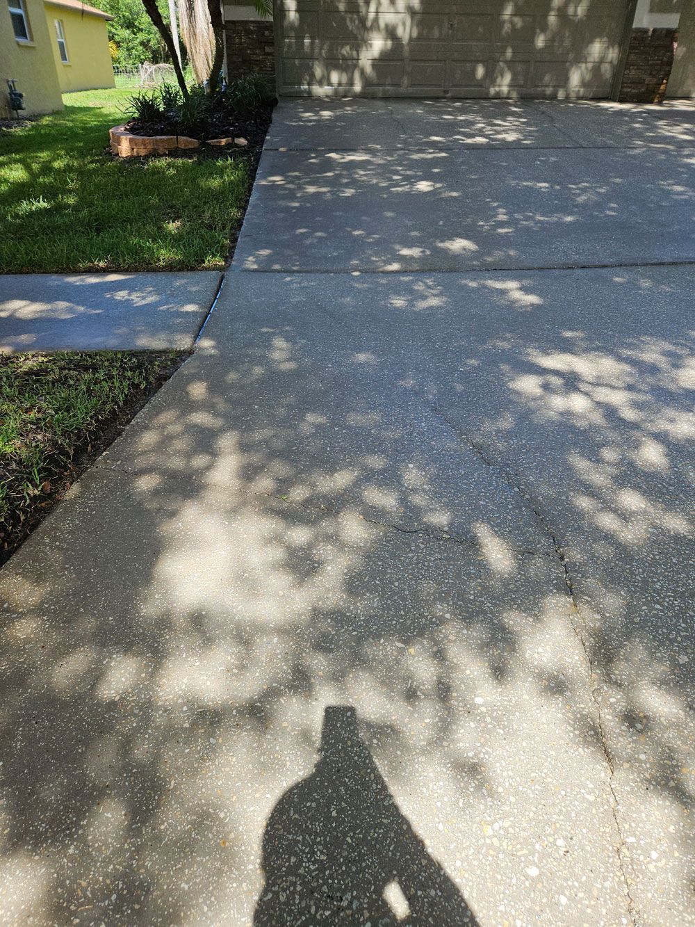 Driveway and front walkway in dappled sunlight, with a house entrance and lawn beside it.