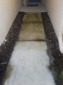 Narrow outdoor walkway with a raised, worn central strip and dark gravel borders beside white walls.