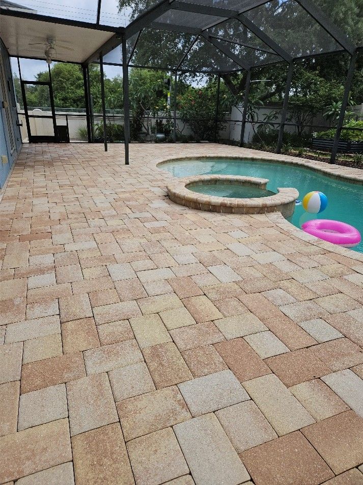 Screened backyard patio with a small pool, tan brick pavers, and a colorful beach ball and float toys.