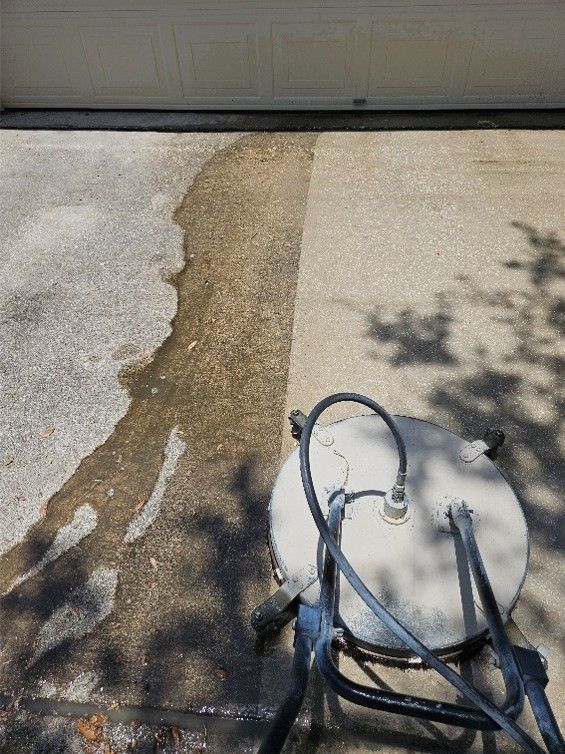 Wet concrete driveway with a pressure washer and a darker cleaned path near the garage door