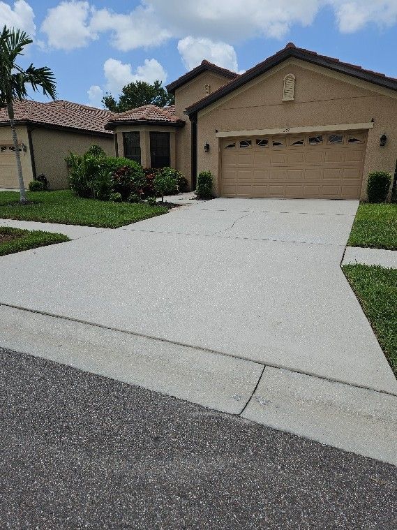 Suburban house with a two-car garage and a wide concrete driveway under a partly cloudy sky