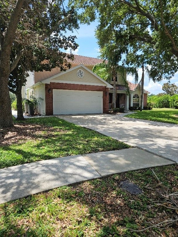 Suburban house with two-car garage, driveway, and palm trees under a sunny sky