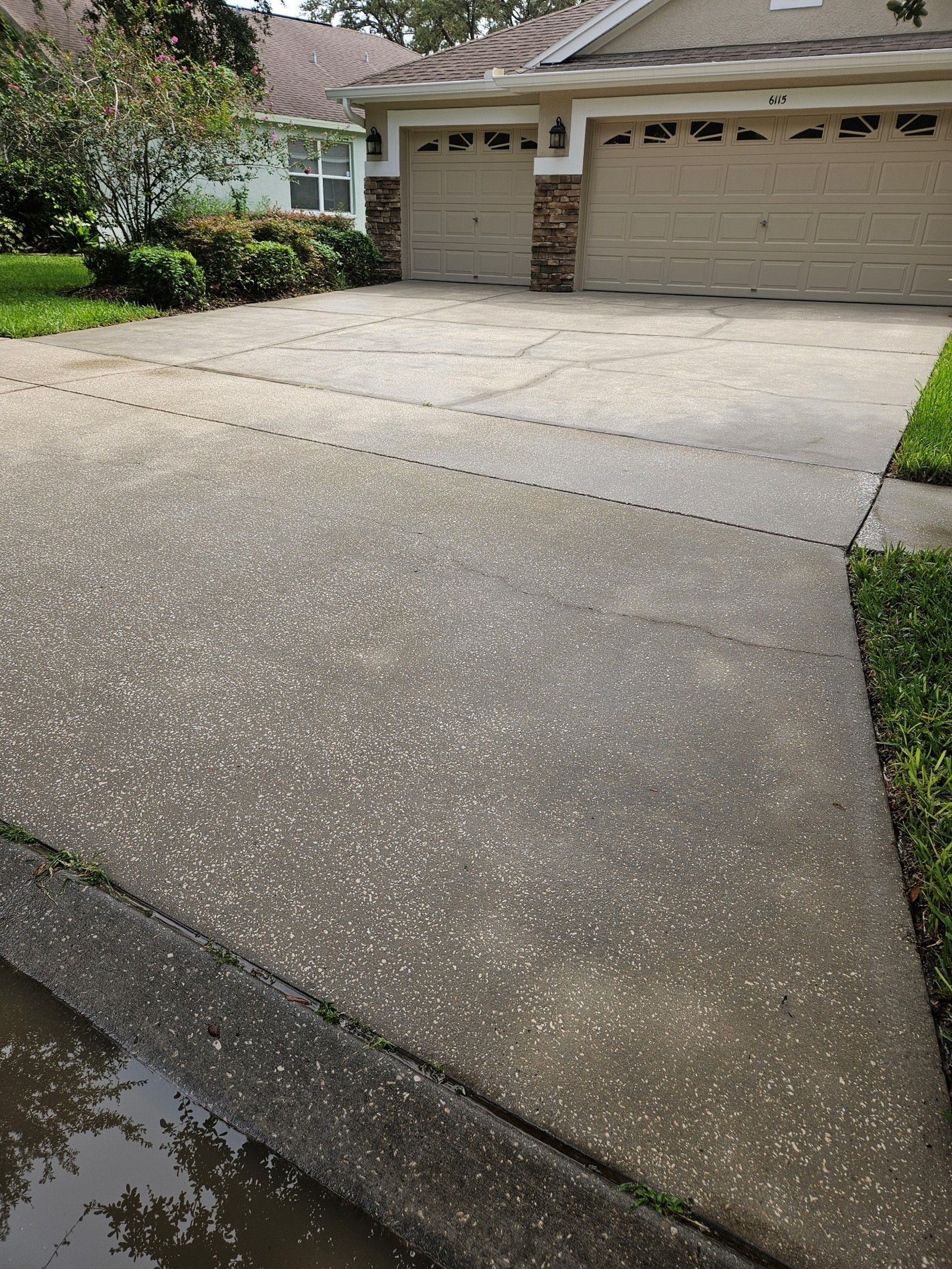 A concrete driveway in front of a house, covered in a light dusting of white hail or snow.