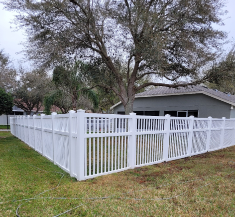 White vinyl fence around a gray house with a large tree and green lawn