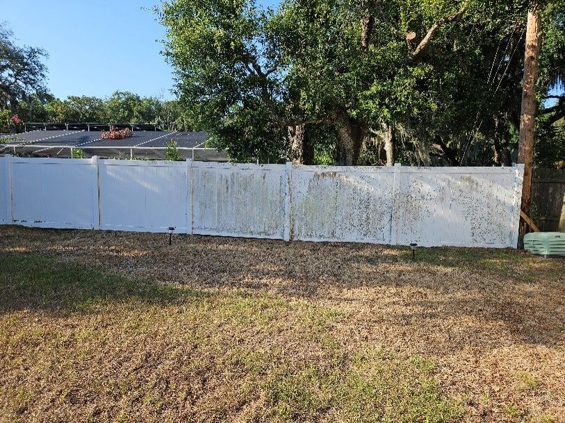 White fence across a grassy yard with trees and a house in the background