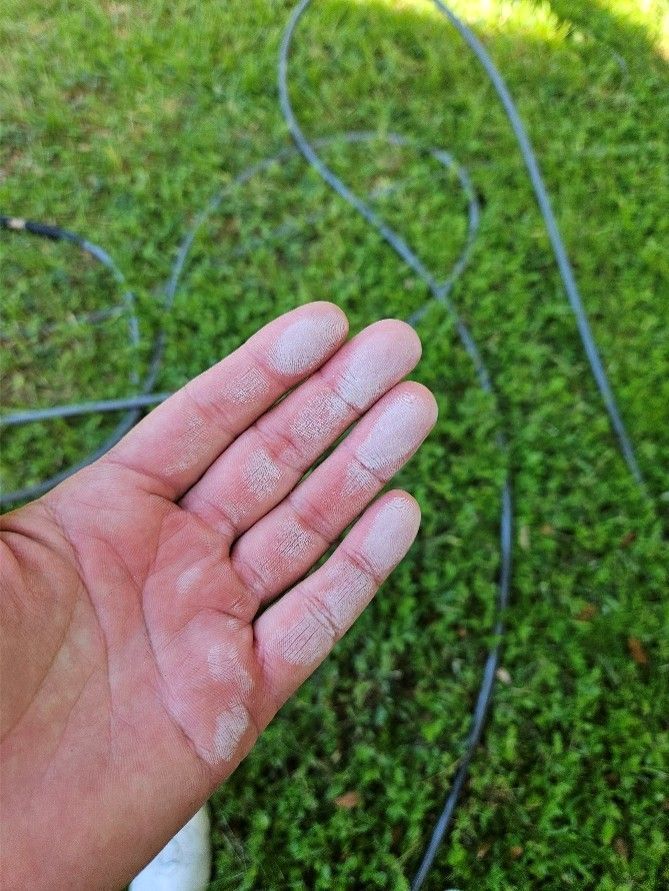 Open hand with white powder on fingers over green grass and black hose cords
