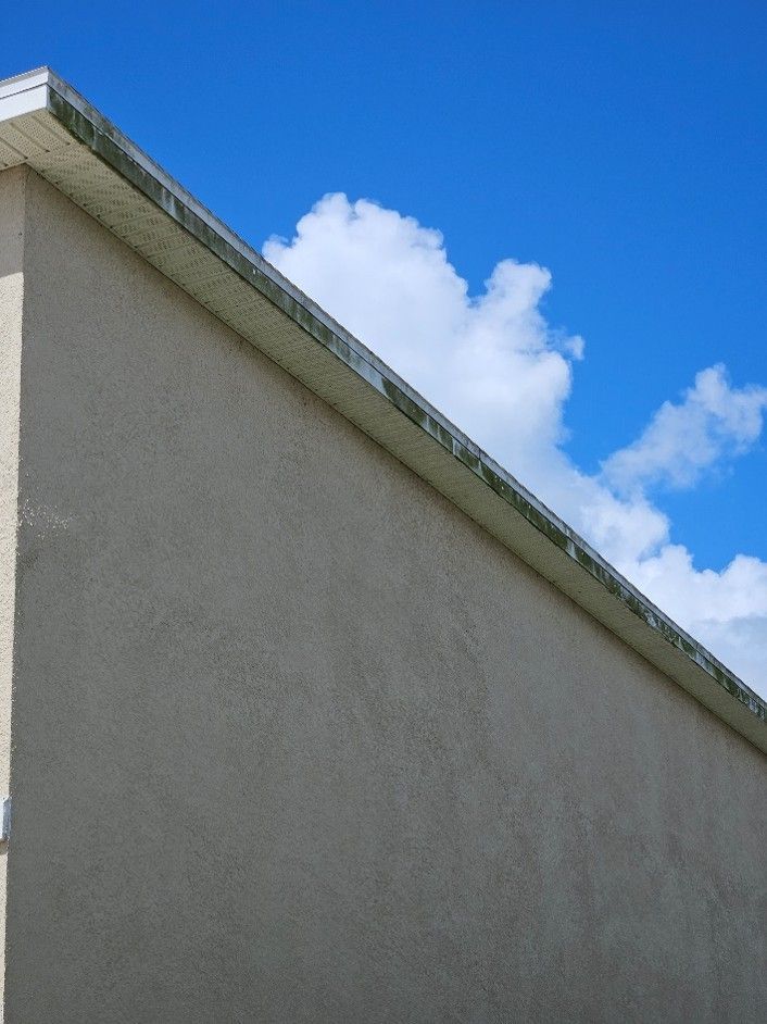 Gray building wall with green roof edge against a blue sky with clouds