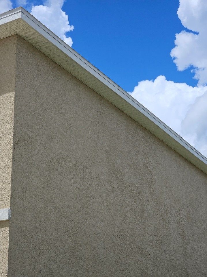 Beige stucco house wall and roofline against a bright blue sky with clouds