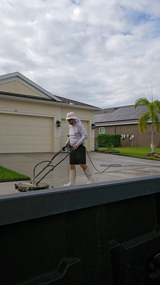 Person power-washing a driveway in a suburban neighborhood.
