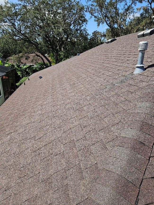 Sunlit shingled roof with a vent pipe and trees in the background