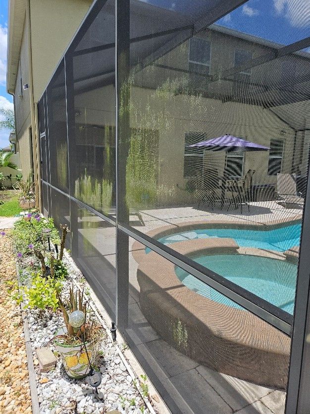Screened patio with a turquoise pool, striped umbrella, and garden beds beside a house