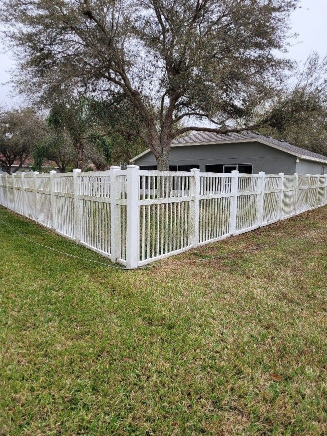 White picket fence around a gray house in a grassy yard with trees overhead