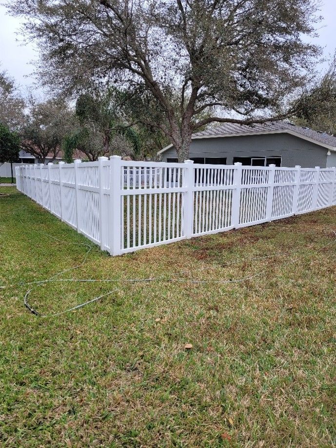 White vinyl fence around a grassy yard beside a gray house and large trees