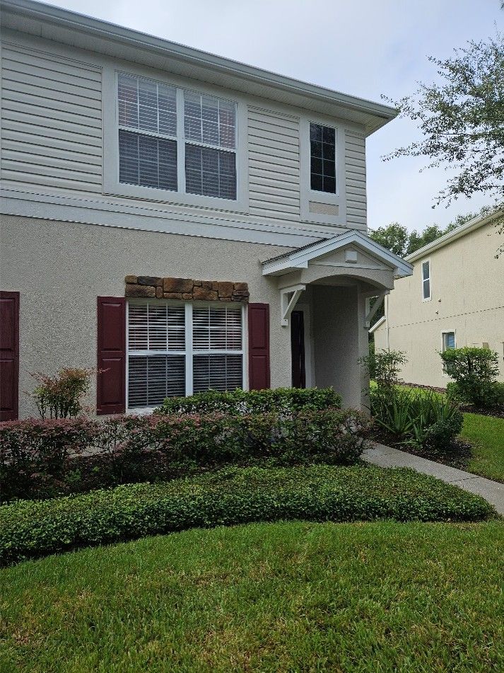 Two-story beige house with red shutters, white trim, and a front porch beside a green lawn