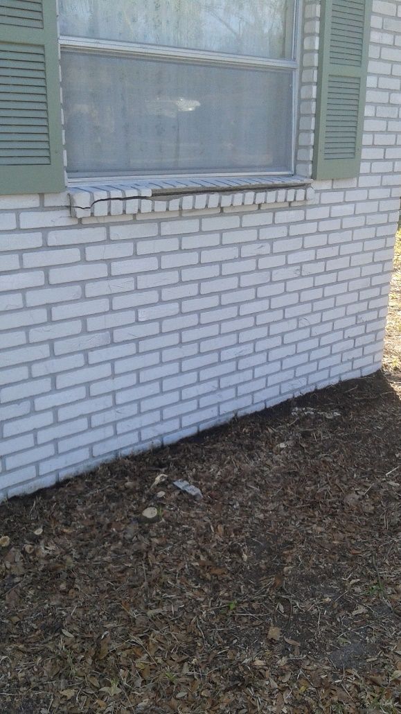 White brick house wall with a window and the ground below covered in leaves or mulch