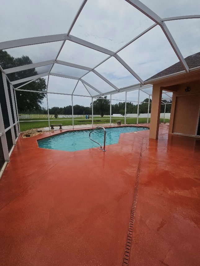 Covered backyard pool with red patio and screened enclosure on a cloudy day