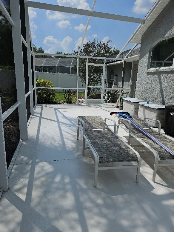 Sunlit backyard patio with white lounge chairs, a glass table, and a screened pergola.