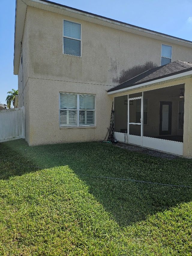 Backyard view of a beige two-story house with green lawn and a covered patio