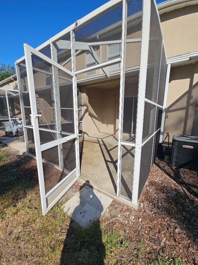 Open white screen door frame leaning against a beige house exterior in sunlight