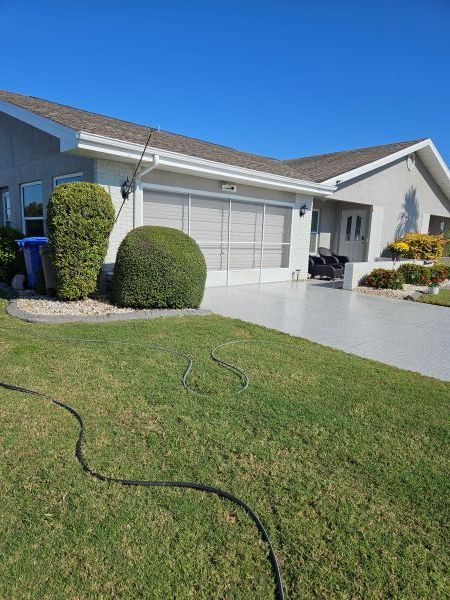 Suburban house with white garage, trimmed shrubs, and a green lawn under a clear blue sky