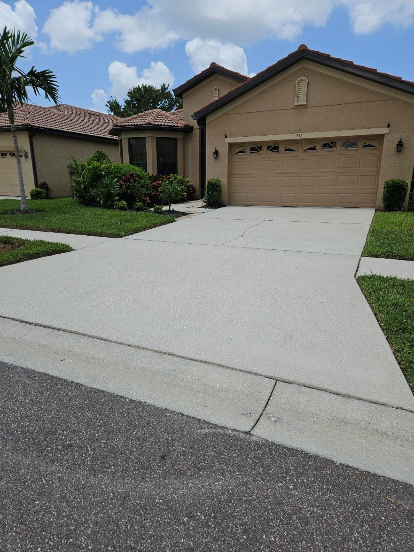 Suburban house with a beige garage, front entry, and a wide concrete driveway under a partly cloudy sky