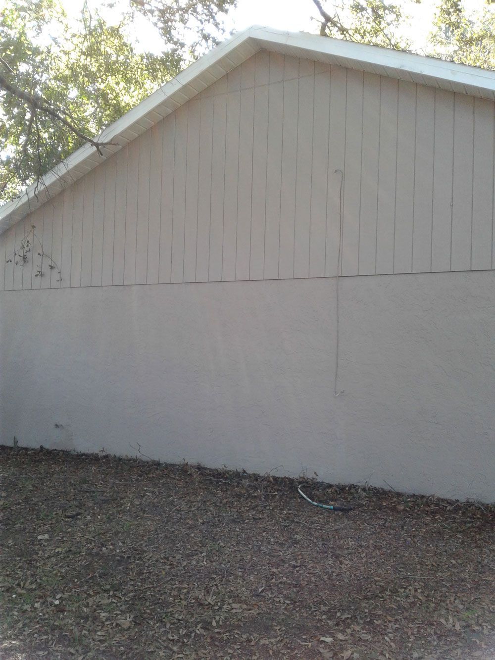 Side view of a light-colored wooden shed with a gabled roof and gravel ground in front