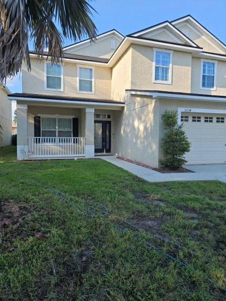 Two-story beige house with a porch and attached garage on a grassy lot.