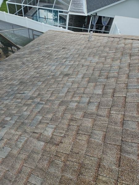 Overhead view of a weathered asphalt shingle roof. The shingles are various shades of brown and gray.