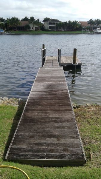 Wooden dock extends into water with houses in the background. Green grass lines the dock's edge.