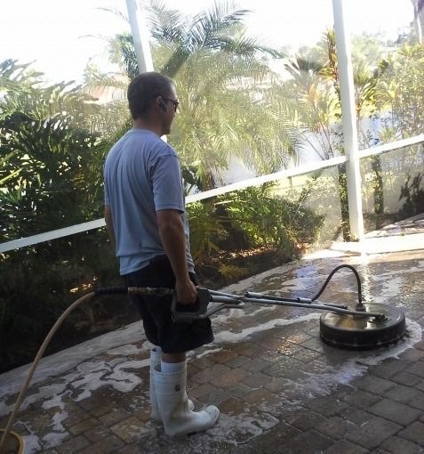 Man power washing a brick patio with a circular surface cleaner.