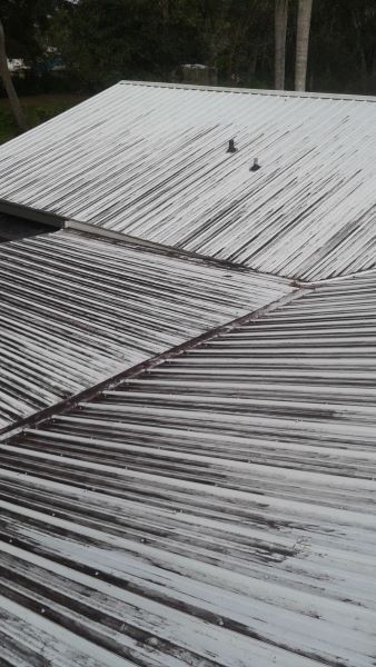 Corrugated metal roof with light-colored coating and two bolts.
