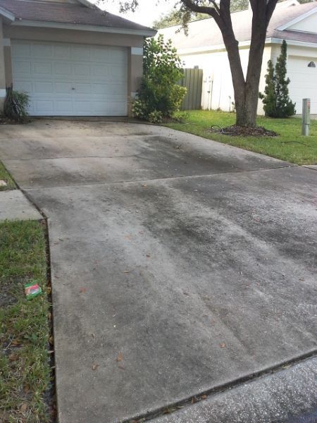 Driveway with concrete sections, stained, leading to a garage door. Lawn on either side, tree in the yard.