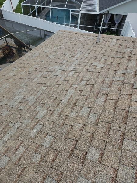 Tan and light-brown asphalt shingle roof. White fence and pool area visible in the background.