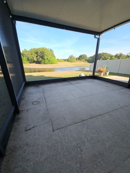 Patio enclosed by dark frames with view of pond, trees, and blue sky. Concrete floor.