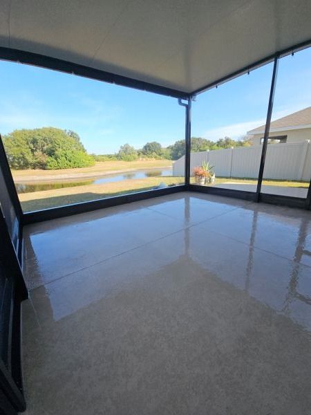 Sunroom with clear glass walls overlooking a pond and yard on a sunny day.
