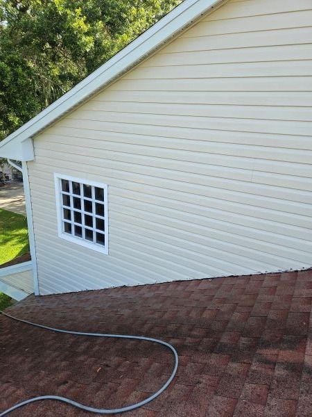 Side view of a house with beige siding, a small window, and a brown shingle roof.