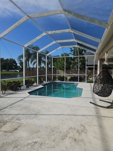 Pool enclosed by white screen, under a bright blue sky. Black hanging chair on the right.