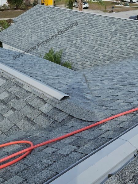 Roofs with grey shingles, an orange hose, and a cleaning company logo.