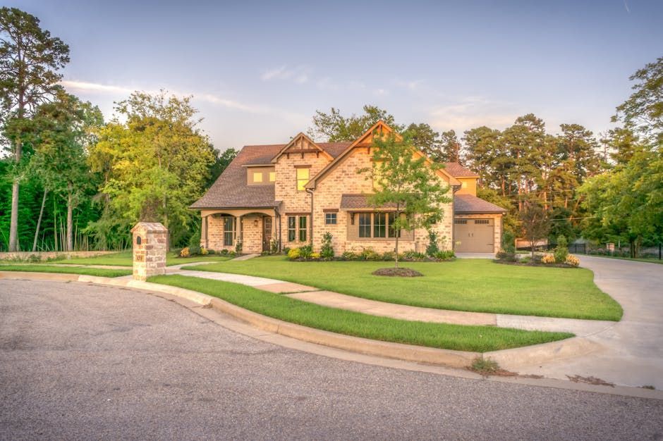 Two-story brick house with a manicured lawn and driveway, surrounded by trees, viewed on a sunny day.