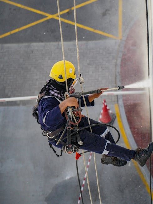 A man in a yellow helmet is spraying water on a building