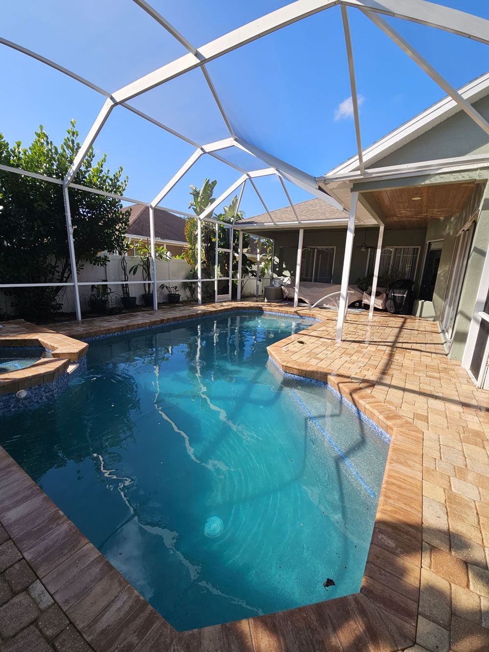 Screened backyard pool with blue water, brick patio, and white enclosure under a clear sky