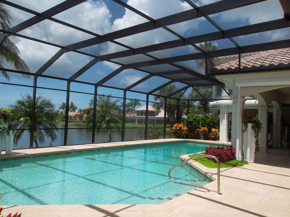 Screened backyard pool with patio, palm trees, and water view under a glass enclosure
