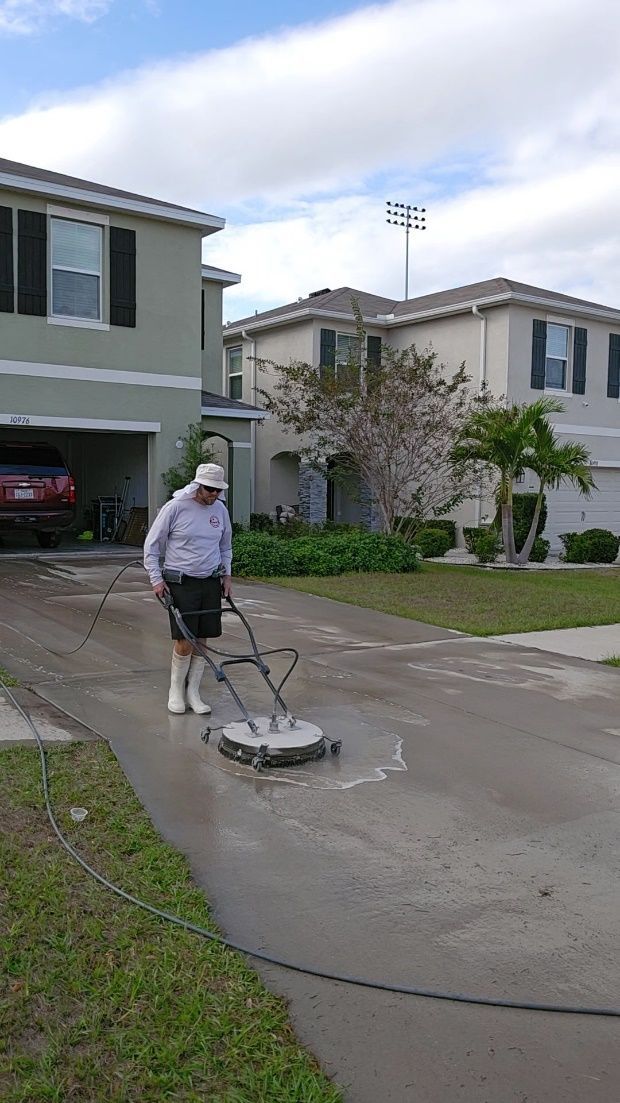 Person pressure-washes a driveway in front of suburban houses.